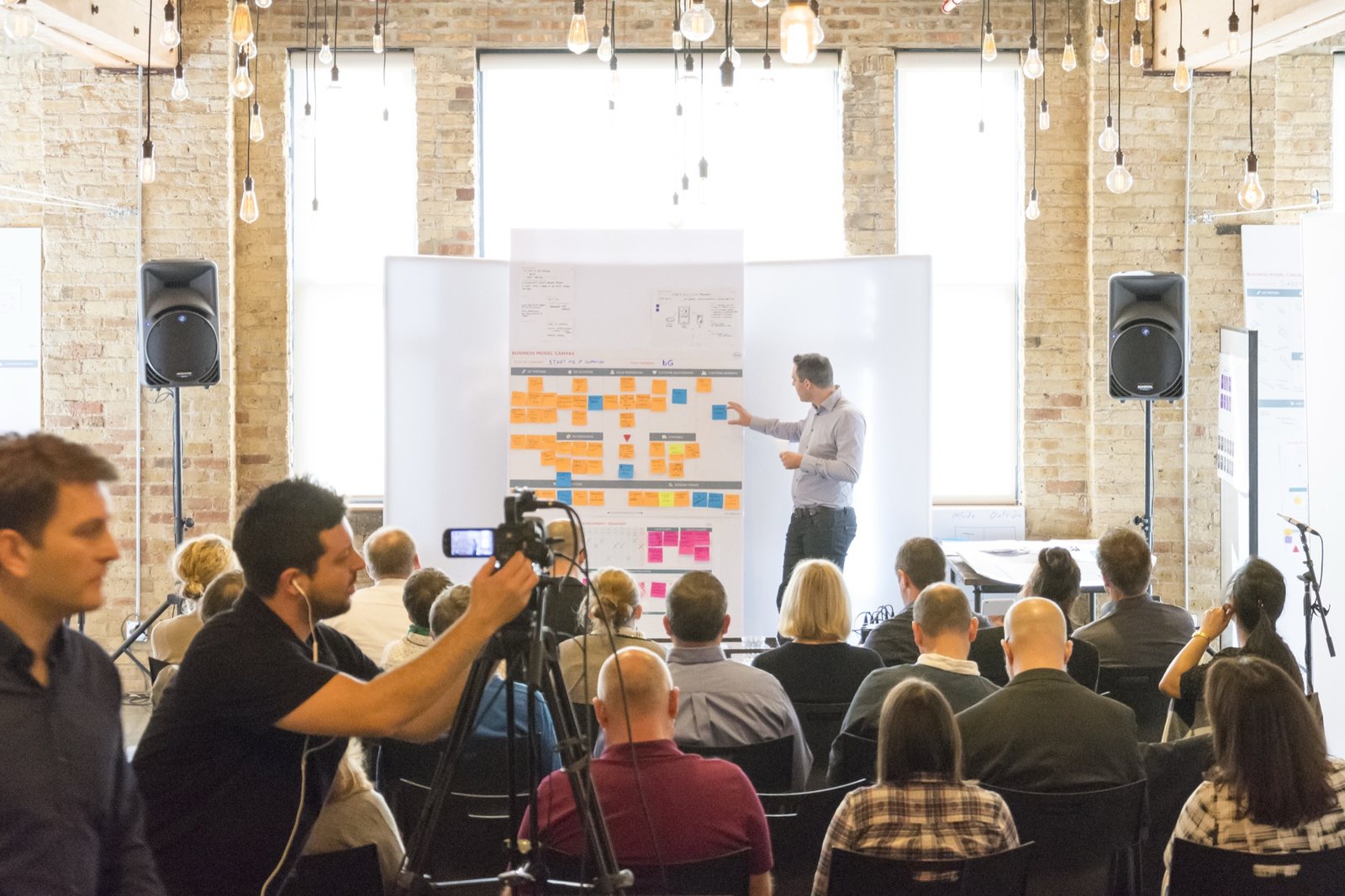 A facilitator presenting at a wall of work to a seated group